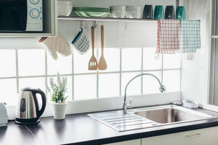 Home kitchen interior. Cooking utensils on a railing system and shelf with dishes above a window.の写真素材