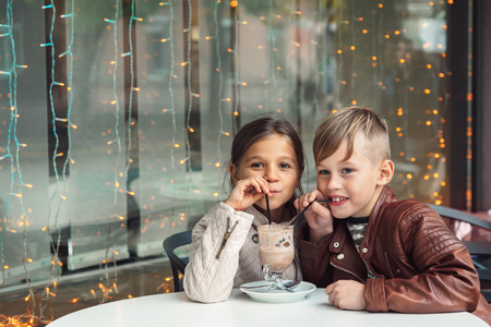 Children having fun in outdoor cafe. Kids talking and drinking cocoa for the breakfast in the city street in autumn.の写真素材