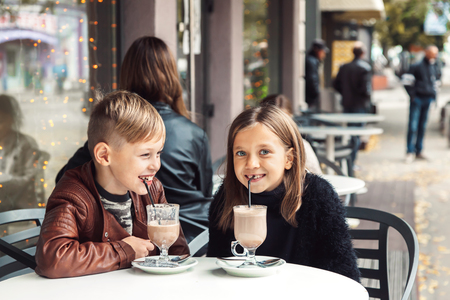 Children having fun in outdoor cafe. Kids talking and eating dessert in the city street. Autumn weekend with friends.の写真素材