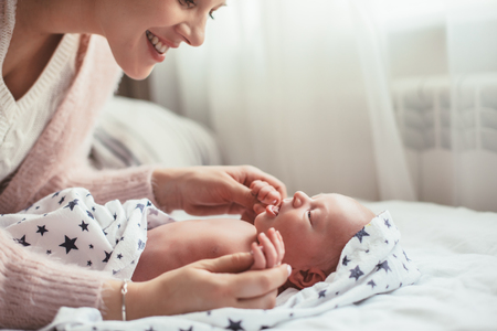 Home portrait of a newborn baby with mother on the bed.の写真素材