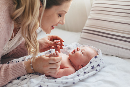 Home portrait of a newborn baby with mother on the bed.の写真素材