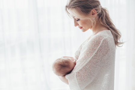 Bright portrait of a mom breast feeding baby over window lighting.の写真素材