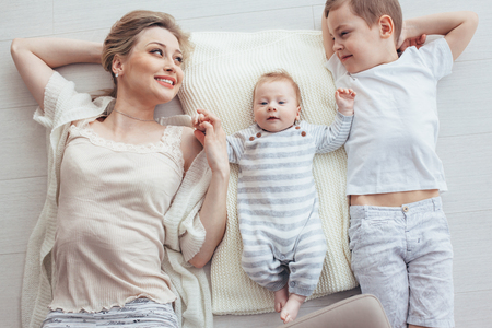 Young mom with her 5 years old son and 2 month old baby are relaxing and playing on the floor, top view from aboveの写真素材