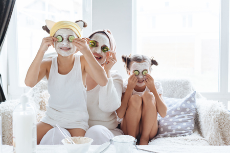 Mom with her daughters making clay face mask. Mother with children doing beauty treatment together. Morning skin care routine.の写真素材