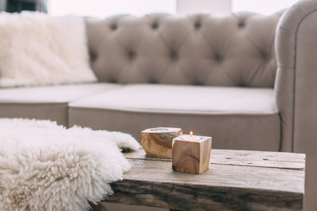 Still life details of nordic living room. Sheep skin rug on rustic bench by the sofa with fur cushions. Cozy winter scene in Scandinavian interior.の写真素材