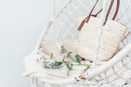 Summer hygge scene with hammock chair, book and flowers. Cozy place for weekend relax in the garden.