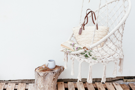 Summer hygge scene with hammock chair, book and flowers. Cozy place for weekend relax in the garden.