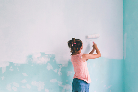 Preteen child painting the wall in her room in blue and white colors. Young girl making interior renovation at home.の写真素材