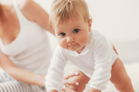 Portrait of loving mom playing with her 8 months old baby in bedroom, making first steps togetherの写真素材