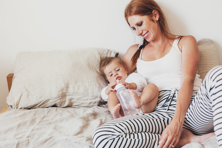 Portrait of beautiful loving mom feeding her 8 months old baby with bottle in bedroomの写真素材