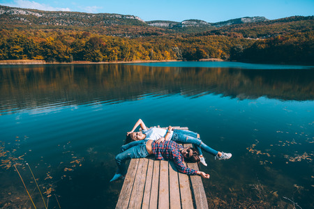 Two friends resting on peer and enjoying lake view in autumn. Good sunny day for resting outdoors and travel.の写真素材
