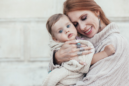 Portrait of beautiful mom holding on hands her 8 months old baby. Both dressed in warm winter...