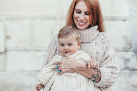 Portrait of beautiful mom holding on hands her 8 months old baby. Both dressed in warm winter knitted clothing.の写真素材