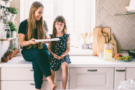 Mom with her child sitting on the kitchen table and eating candies. Mother with daughter having breakfast at home. Happy lifestyle family moments.の写真素材