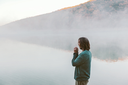 Man in sweater standing and looking at fog. Cold morning by the lake.の写真素材
