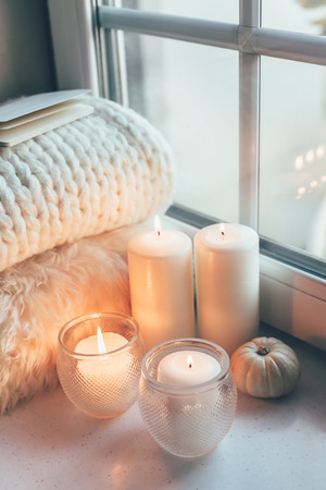 Warm and cosy hygge concept with white sweater and candles on a windowsillの写真素材