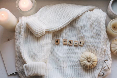 Warm and cosy hygge flatlay with white sweater and candles on a windowsill