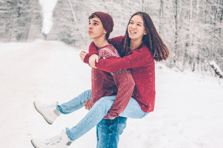 Photo of teenage friends in red Christmas sweaters playing in snow one winter day. People having...
