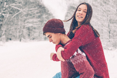 Photo of teenage friends in red Christmas sweaters playing in snow one winter day. People having good time on the January weekends.の写真素材