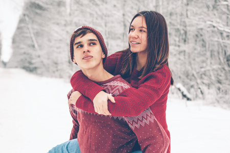 Photo of teenage friends in red Christmas sweaters playing in snow one winter day. People having good time on the January weekends.の写真素材