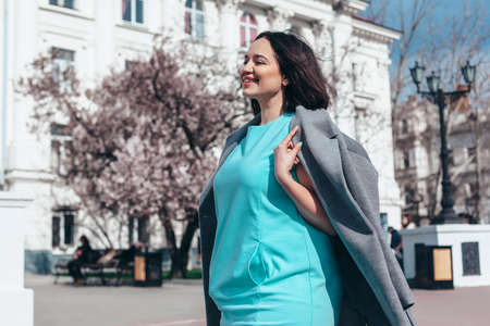 Beauitful plus size model wearing blue dress and grey coat walking by blooming spring tree outdoor on the city street.の写真素材