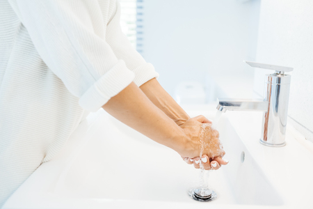 Closeup photo of person washing hands in white clean basin in home washroomの写真素材