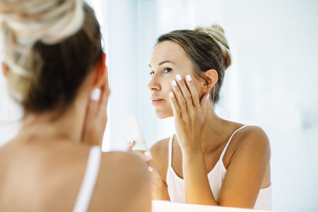 Photo of woman applying face cream after daily shower. Making everyday morning routine in bathroom.の写真素材