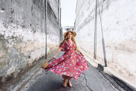 Boho girl in maxi dress and straw hat walking on the Asia city street. Travelling in Phuket Old Town in Thailand.の写真素材