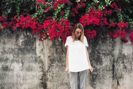 Hipster girl wearing blank white t-shirt posing against gray street wall with spring flowers, blank mockup for tshirt print storeの写真素材