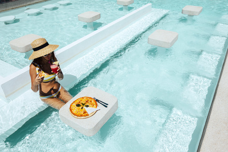 Girl relaxing and eating pizza and drinking cocktail in the hotel pool. Luxury tropical beach lifestyle.の写真素材