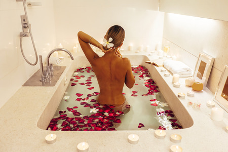 Woman relaxing in luxury bath decorated with candles and flower petals. Organic skin care in...