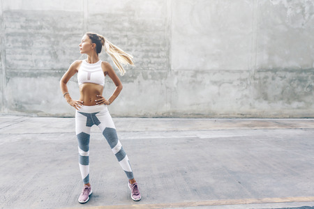 Fitness model in sportswear posing on the city street over gray concrete background. Outdoor sports clothing and shoes, urban style.の写真素材
