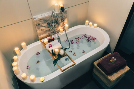 Prepared luxury spa bath decorated with flowers and candles, with wooden tray on itの写真素材
