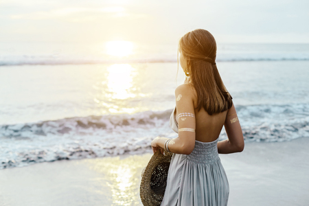 Back view of young teenage girl thinking while looking at horizon over shore on sunsetの写真素材