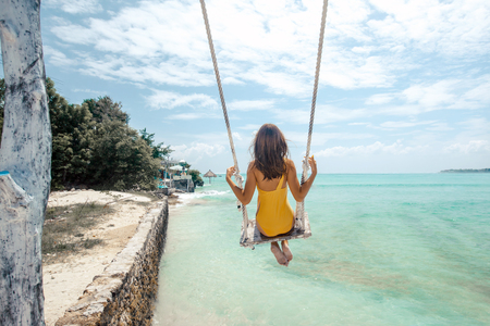 Back view of teenage girl hanging on beach swings. Summer vacation on paradise island.の写真素材