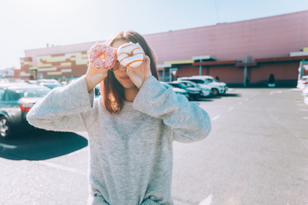Teenage girl eating donut outside. Teenager with trendy street food near shopping mall.の写真素材