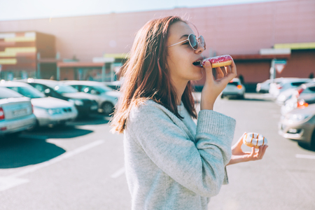 Teenage girl eating donut outside. Teenager with trendy street food near shopping mall.の写真素材