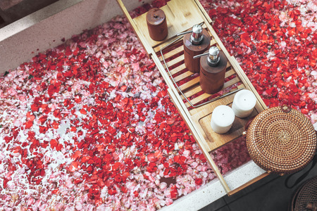 Bathtub with flower petals and beauty products on wooden tray. Organic spa relaxation in luxury Bali outdoor bath.の写真素材