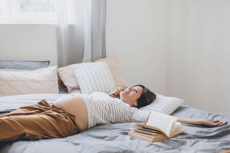 Calm home portrait of pregnant woman reading book while resting on the bed