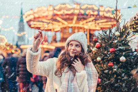 Girl walking in Christmas market decorated with holiday lights in the evening. Feeling happy in big city. Spending winter vacations in Red square, Moscow, Russia.の写真素材