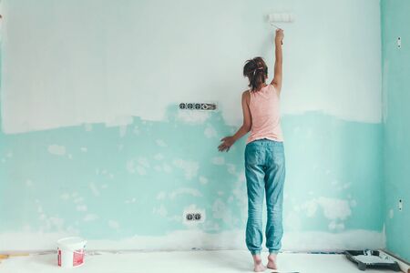Preteen child painting the wall in her room in blue and white colors. Young girl making interior renovation at home.の写真素材
