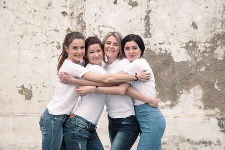 Group of four young diverse girls wearing blank white tshirt and jeans posing against rough street wall, fashion urban clothing style, mockup for t-shirt print storeの写真素材