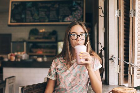 Positive teen girl enjoying sweet smoothie while spending time in loft cafeの写真素材