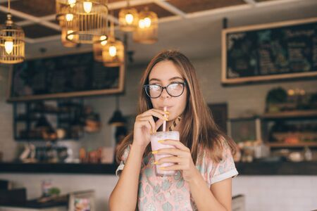 Positive teen girl enjoying sweet smoothie while spending time in loft cafeの写真素材