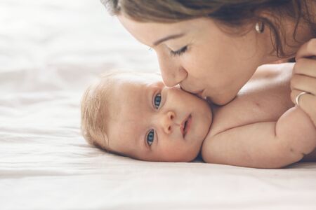 Loving mom carying of her newborn baby at home. Mother kissing her little 2 months old son.