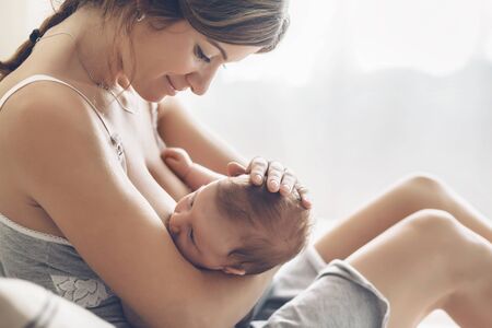 Loving mom breastfeeding her newborn baby. Bright portrait of happy mum holding infant child on...