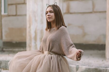 Sepia filtered photo of teen girl wearing brown tulle skirt and knitted oversized sweater posing in city street.の写真素材