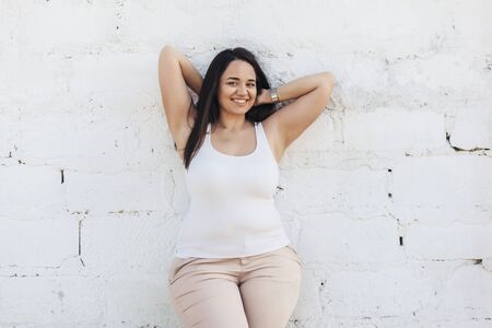 Beautiful plus size female model dressed in blank white shirt posing over brick wall backgroundの写真素材