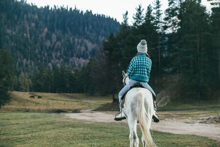Teen girl riding a white horse on meadow by forest in natureの写真素材