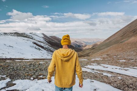 Rear view of young traveler standing on mountain and looking at beautiful landscape. Cold weather,...